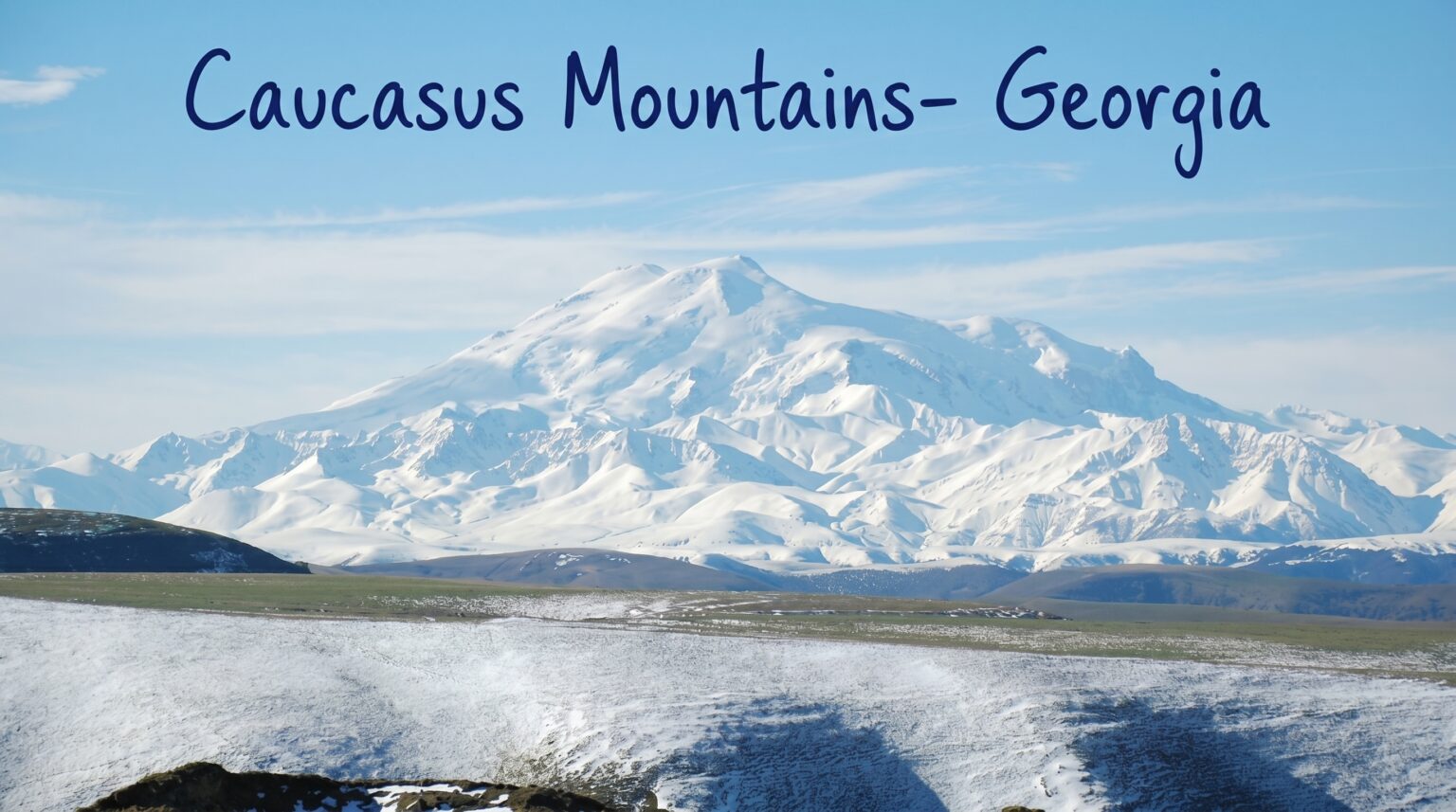 A massive snow-covered mountain peak rises against a bright blue sky, with rolling grassy hills in the foreground and the text "Caucasus Mountains- Georgia" written across the top.